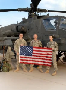 Soldiers holding American flag in front of helicopter.